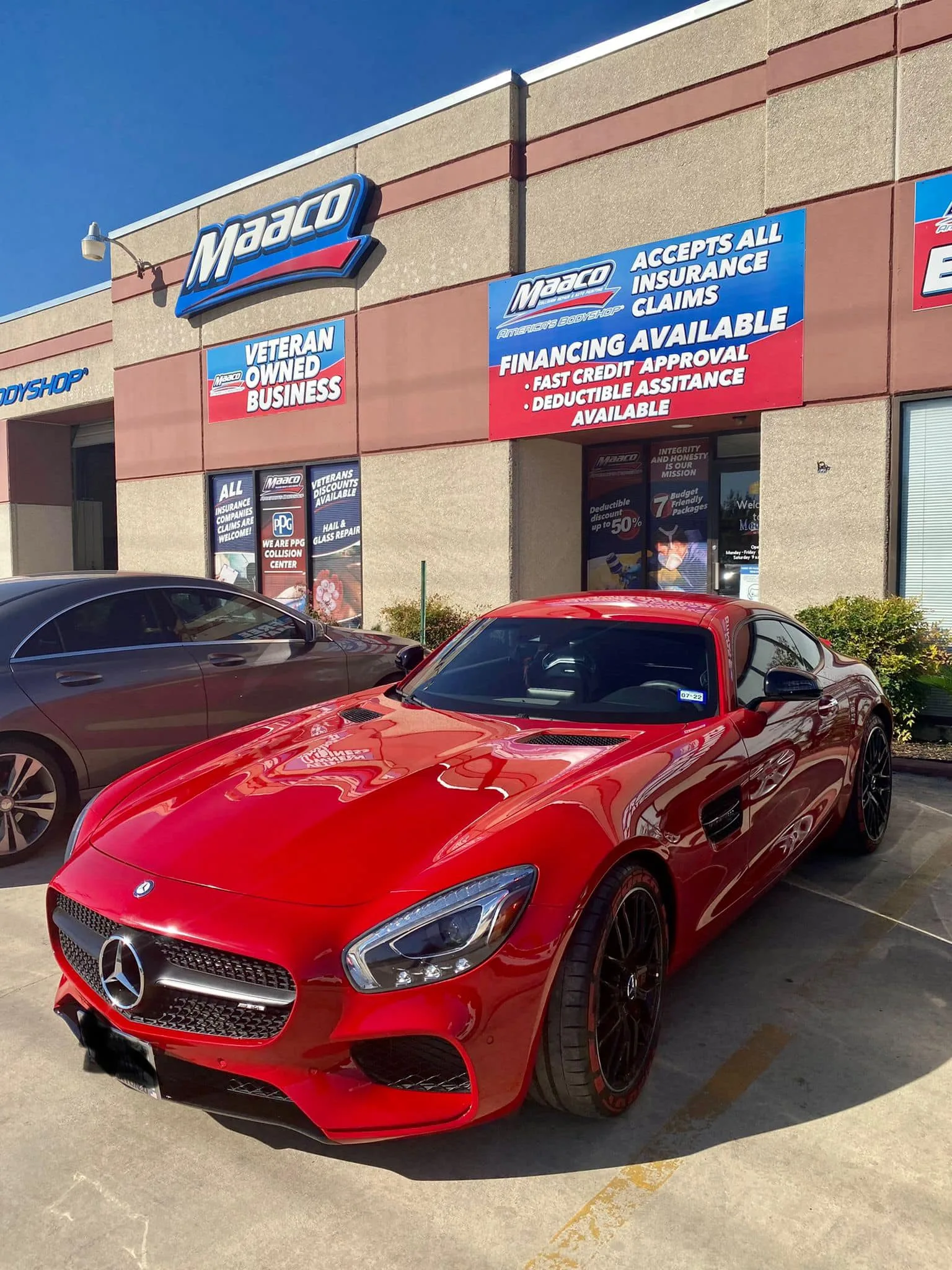 A red sports coupe parked in front of an auto body shop with signage above the entrance.